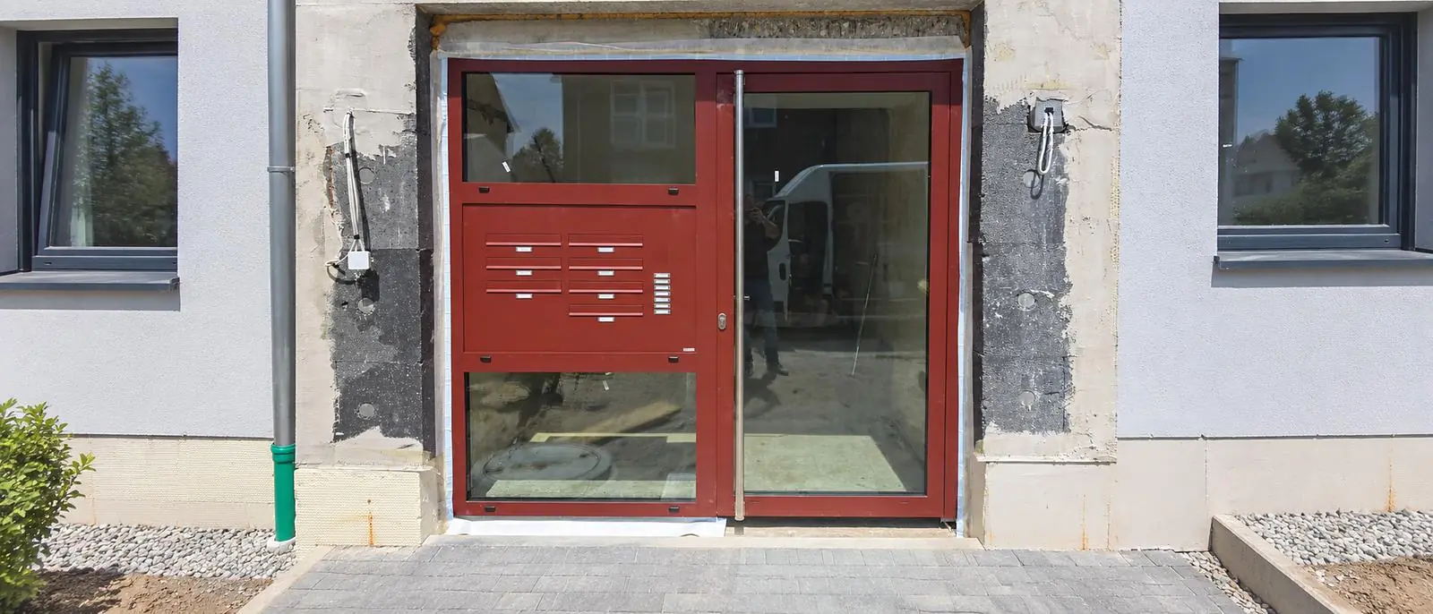 Neue rote Aluminium-Eingangsanlage mit Glas, Briefkasten- und Klingelanlage an einem Mehrfamilienhaus